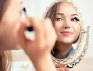 Beauty model teenage girl looking in the mirror and applying mascara make up. Beautiful young woman apply makeup