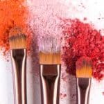Makeup brushes closeup with blush or eyeshadow of pink, red and coral tones sprinkled on white. Make up and female cosmetics background